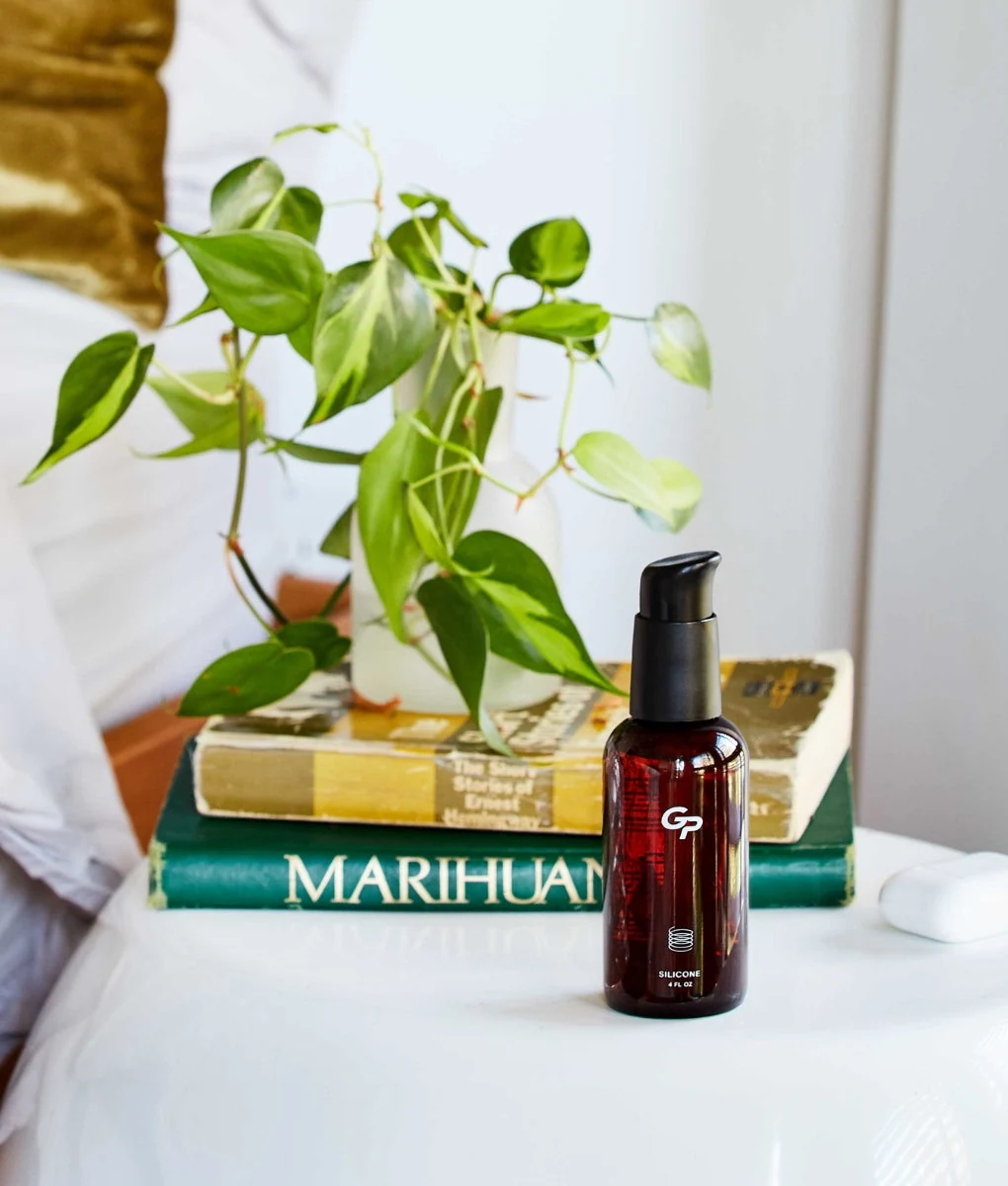 Goodparts silicone lubricant on a bedside table with books and a plant