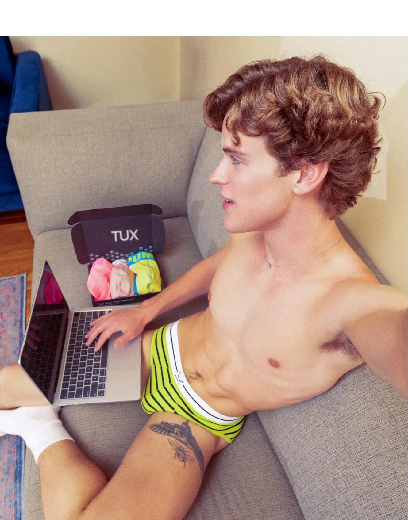 Man on a couch shopping on his laptop, box beside him